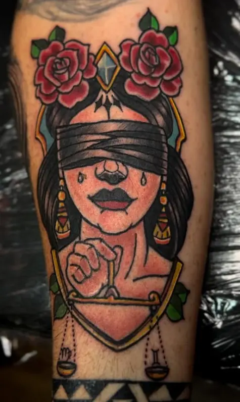 Traditional-style tattoo of a blindfolded woman framed by red roses